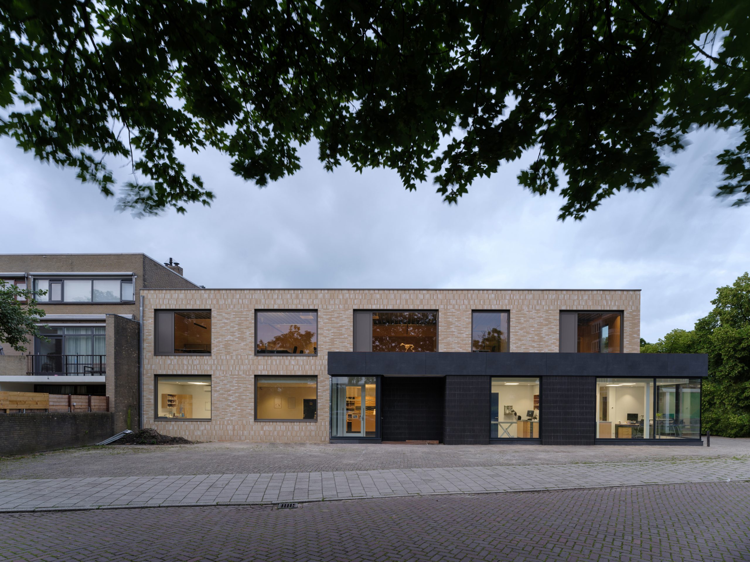 Corner building with glass corner aluminum window frames on ground floor extension. Light colored brick on CLT wood wall and new main entrance to veterinary clinic. Veterinary clinic design for Anicure ‘t Leidse Land in Leiderdorp, designed and built by MOST Architecture, Rotterdam