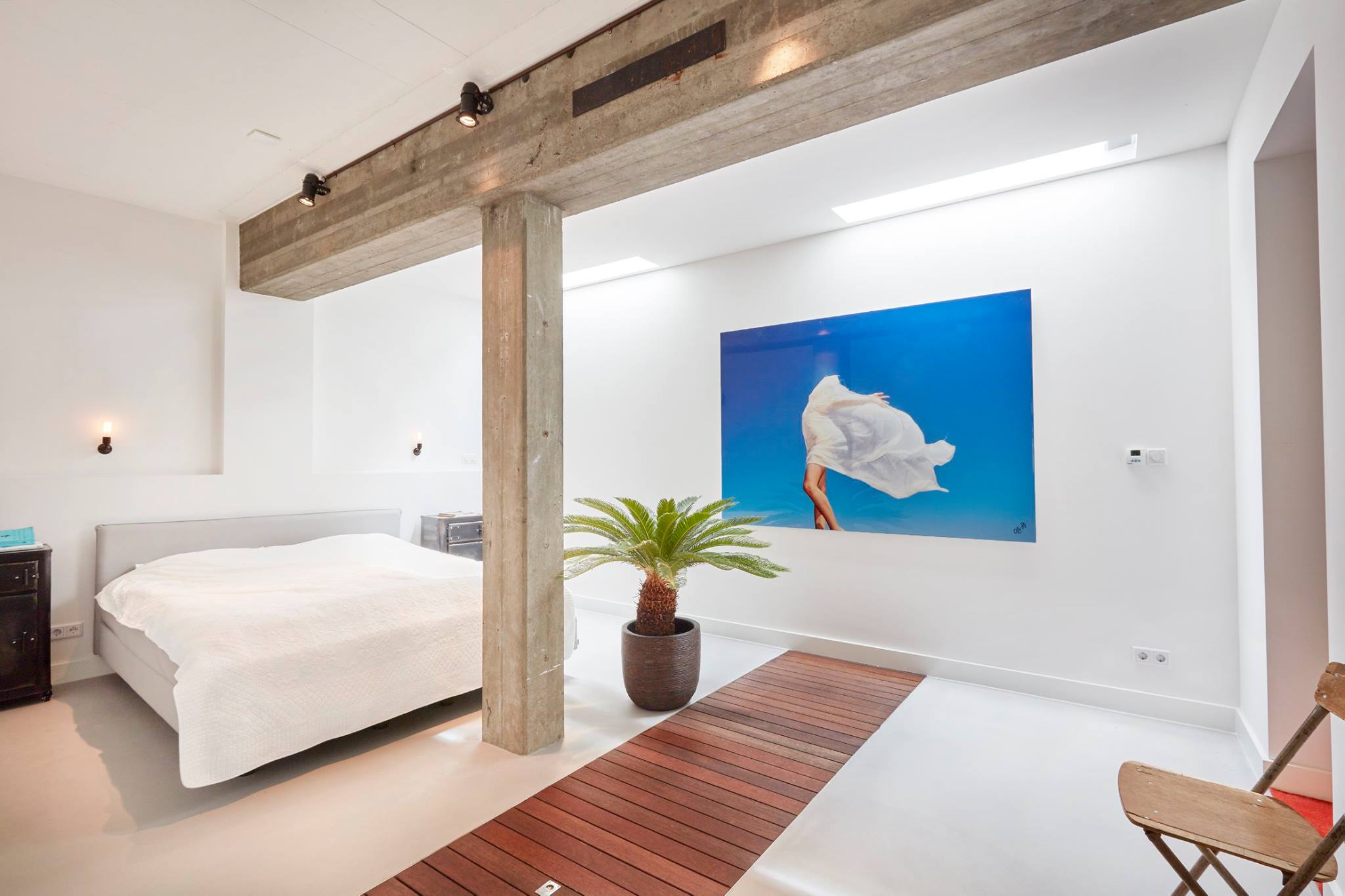 Skylights combined with raw concrete beam and column decorated with palm tree, wooden floor and fantastic art photography. A bespoke and generous master bedroom with meticulous interior design details designed and built by MOST Architecture, Rotterdam