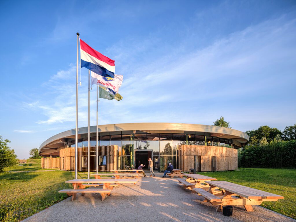 Main entrance approach of the Avonturenhuis Scoutinglandgoed Zeewolde, wooden facade and laminated curved wooden roof with blue sky and building in nature